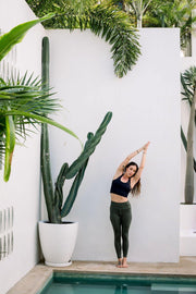 Yogini wearing a black sustainable yoga top and highwaist dark green yoga leggings 